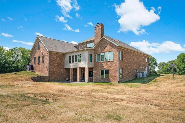 rear view of property featuring a yard, a chimney, cooling unit, and brick siding