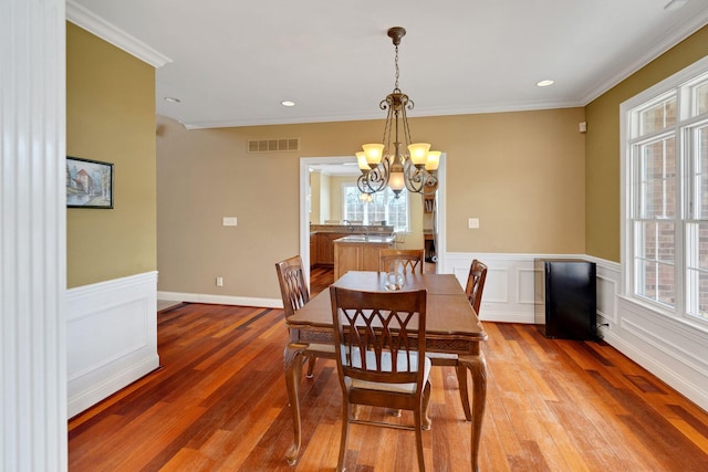 dining space with ornamental molding, wood-type flooring, visible vents, and a notable chandelier