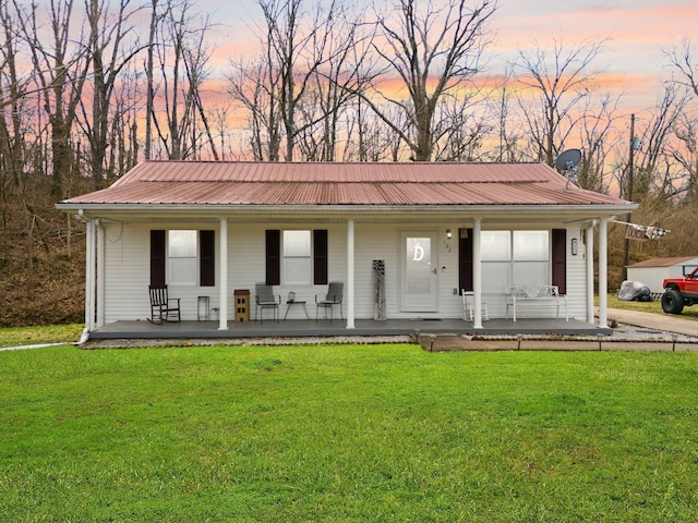 ranch-style home featuring covered porch, metal roof, and a lawn