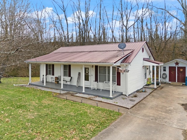 view of front of house with metal roof, covered porch, an outdoor structure, driveway, and a front yard