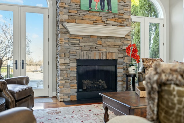 living area with a stone fireplace, french doors, and wood finished floors