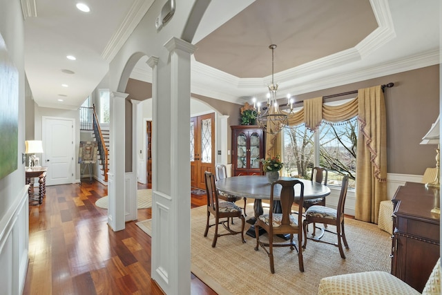 dining room with wood finished floors, ornate columns, arched walkways, wainscoting, and a chandelier