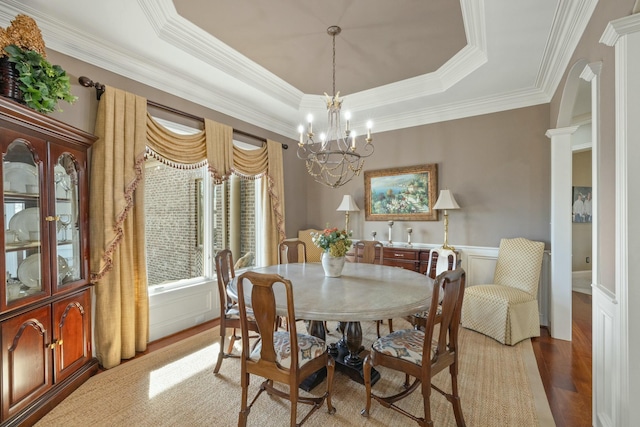 dining room with an inviting chandelier, a tray ceiling, light wood-style flooring, decorative columns, and wainscoting