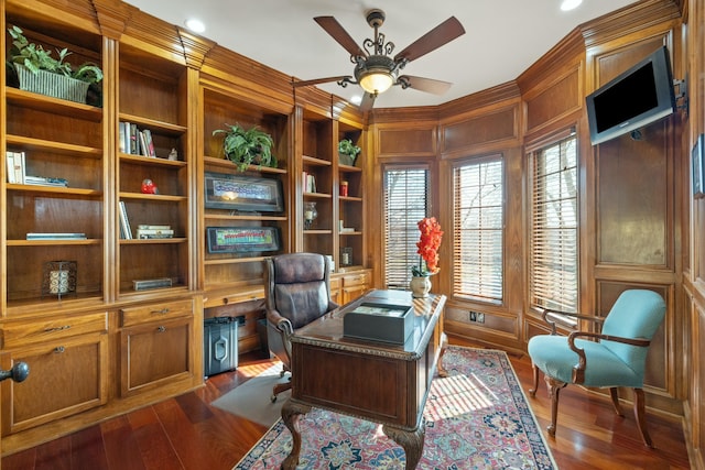 home office featuring dark wood-style floors, wood walls, ceiling fan, and ornamental molding