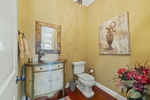 half bath with visible vents, baseboards, toilet, wood finished floors, and vanity