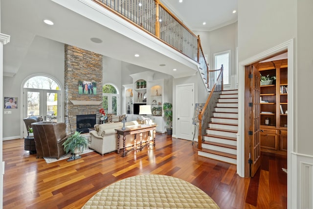 living area with stairway, a high ceiling, a stone fireplace, and hardwood / wood-style flooring