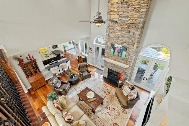 living room featuring a ceiling fan, wood finished floors, a fireplace, french doors, and a towering ceiling