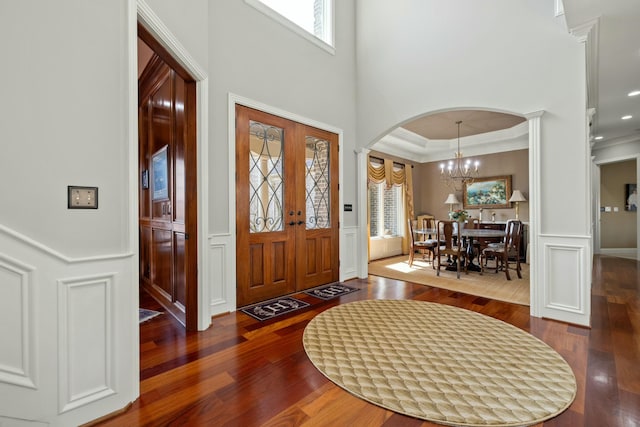 foyer featuring wood finished floors, a wainscoted wall, an inviting chandelier, crown molding, and a decorative wall