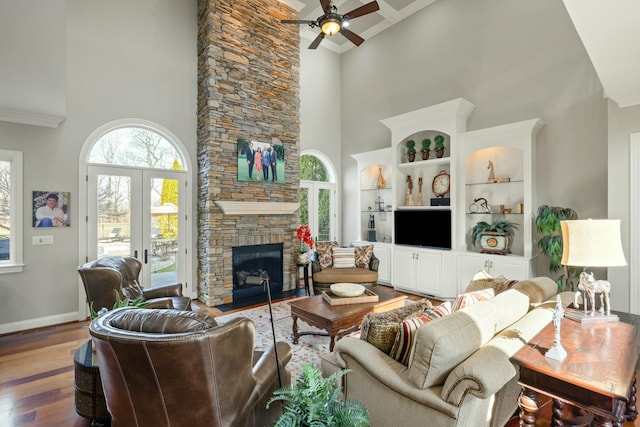 living area featuring a stone fireplace, a high ceiling, baseboards, and wood finished floors