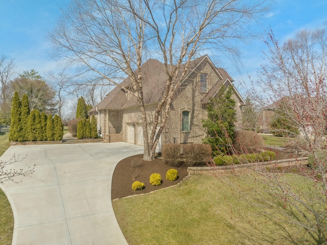 view of side of home featuring an attached garage, brick siding, driveway, and a yard