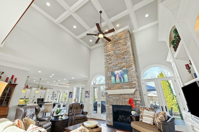 living room with french doors, a high ceiling, a stone fireplace, and ornamental molding