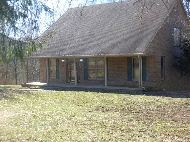 back of property featuring a shingled roof, a patio area, brick siding, and a lawn