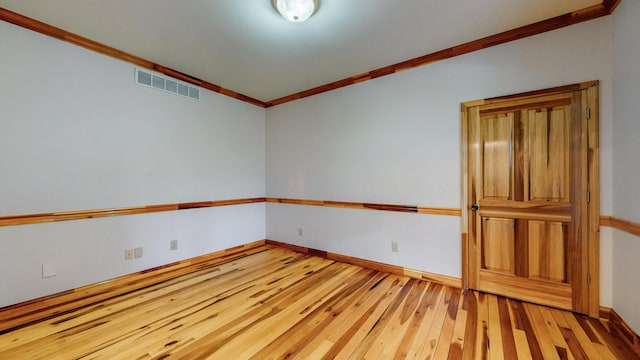 spare room featuring ornamental molding, light wood-type flooring, visible vents, and baseboards