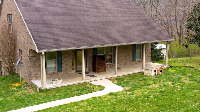 exterior space featuring a patio, brick siding, a front lawn, and a shingled roof