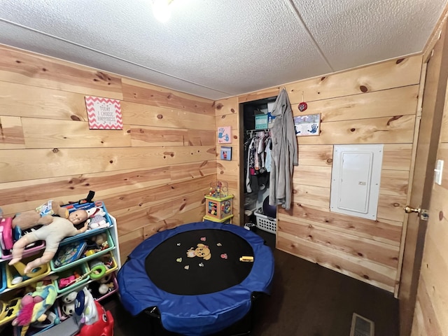 rec room featuring wooden walls, electric panel, visible vents, and a textured ceiling