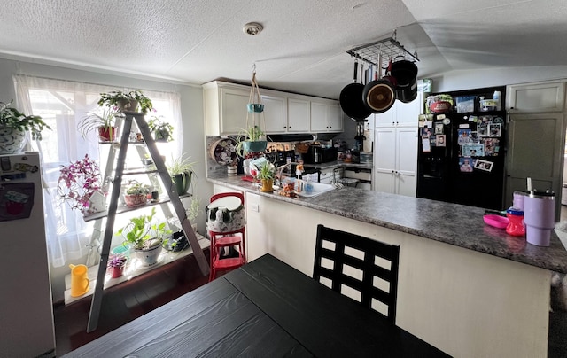 kitchen with refrigerator, lofted ceiling, freestanding refrigerator, white cabinetry, and a textured ceiling