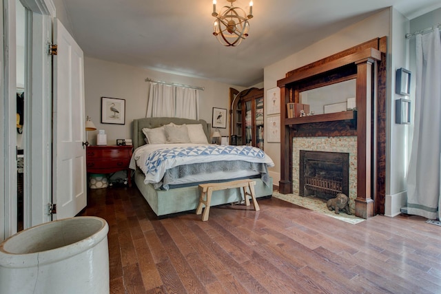 bedroom featuring a notable chandelier, a stone fireplace, and wood finished floors