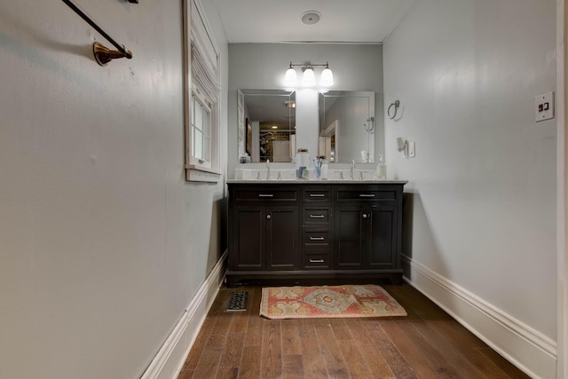 bathroom with a sink, wood finished floors, visible vents, baseboards, and double vanity