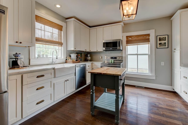 kitchen featuring appliances with stainless steel finishes, dark wood-style flooring, a sink, and baseboards