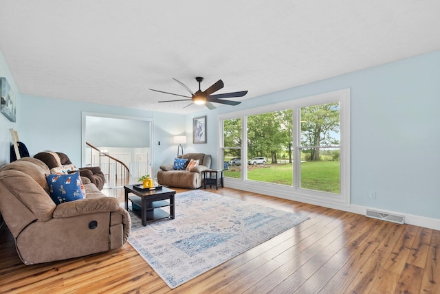 living room featuring visible vents, baseboards, light wood-style flooring, ceiling fan, and stairway