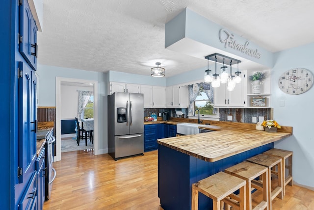 kitchen with stainless steel fridge, butcher block countertops, a breakfast bar, a peninsula, and blue cabinetry