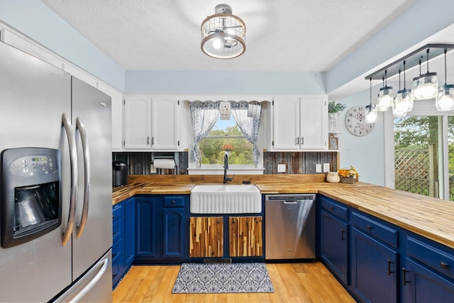 kitchen with stainless steel appliances, butcher block counters, a sink, white cabinets, and blue cabinetry