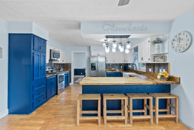 kitchen with a peninsula, blue cabinetry, stainless steel appliances, and a sink