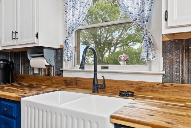 kitchen with blue cabinets, butcher block counters, a sink, and white cabinets