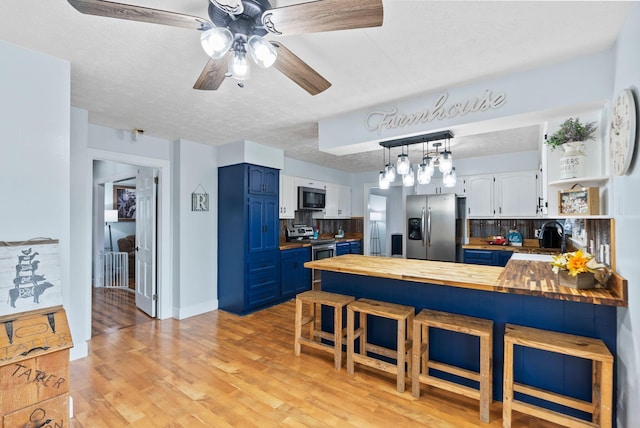 kitchen with stainless steel appliances, butcher block countertops, a peninsula, and blue cabinets