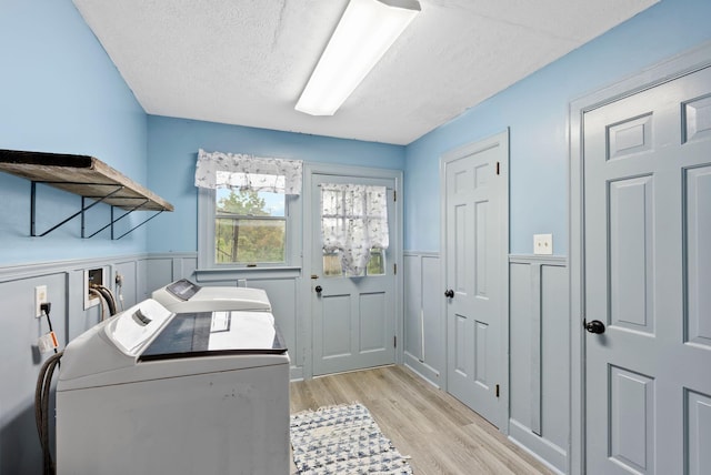 clothes washing area with a textured ceiling, a wainscoted wall, laundry area, washer and dryer, and light wood finished floors