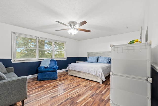 bedroom featuring a ceiling fan, a textured ceiling, baseboards, and wood finished floors