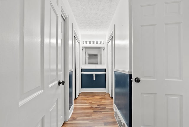 hall featuring light wood-type flooring, baseboards, and a textured ceiling