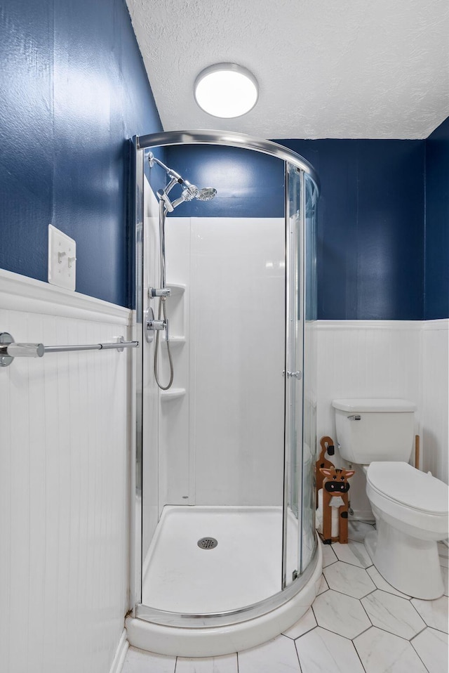 full bath with a stall shower, a wainscoted wall, a textured ceiling, and toilet