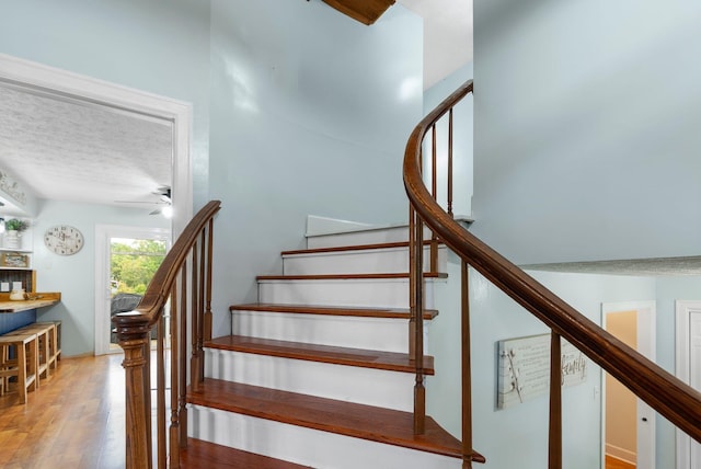 stairs featuring a textured ceiling, wood finished floors, and a ceiling fan