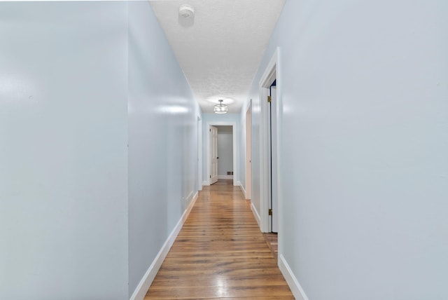 hall featuring baseboards, a textured ceiling, and wood finished floors