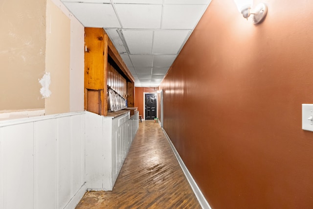 corridor with a drop ceiling, baseboards, and wood finished floors