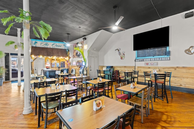 dining area with decorative columns, wooden walls, a ceiling fan, a wainscoted wall, and wood finished floors