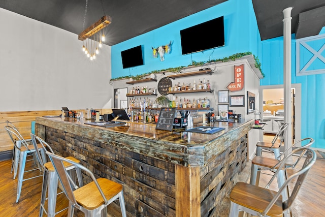 bar featuring a towering ceiling, wood finished floors, and a community bar