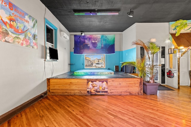 interior space featuring a wall mounted AC, baseboards, and wood finished floors