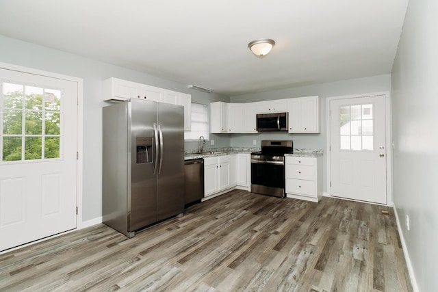 kitchen featuring appliances with stainless steel finishes, plenty of natural light, wood finished floors, and white cabinetry