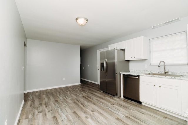 kitchen featuring a sink, white cabinetry, appliances with stainless steel finishes, light wood-type flooring, and light stone countertops