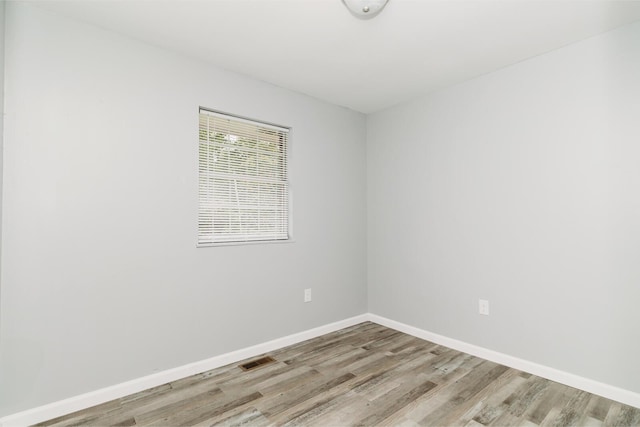 empty room featuring wood finished floors, visible vents, and baseboards