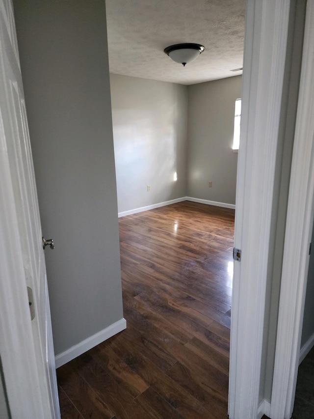 spare room with a textured ceiling, baseboards, and dark wood-style flooring