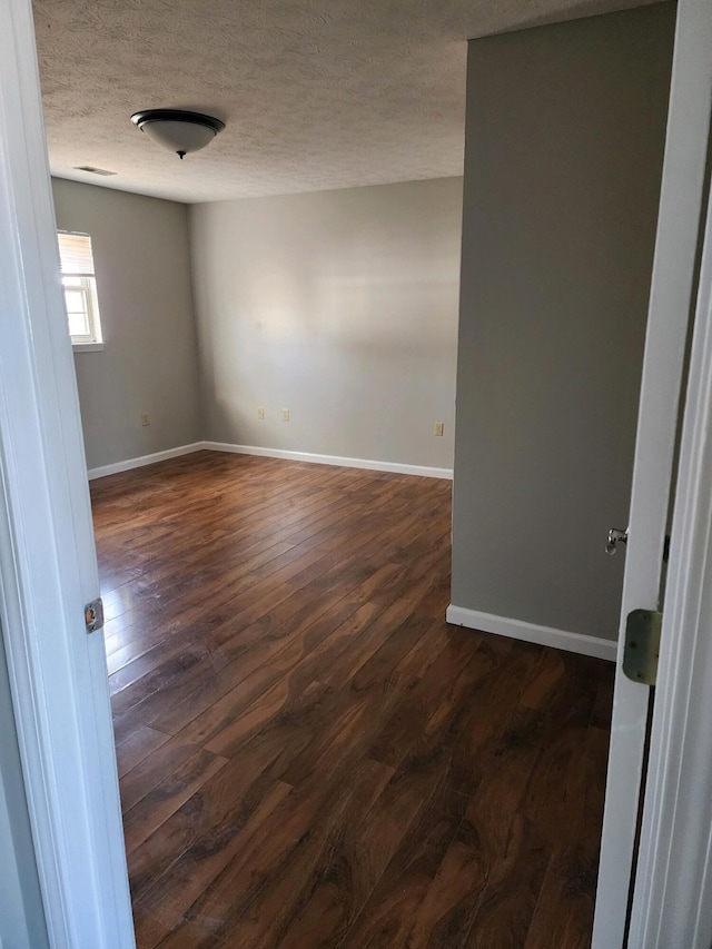 empty room featuring dark wood-style floors, a textured ceiling, and baseboards