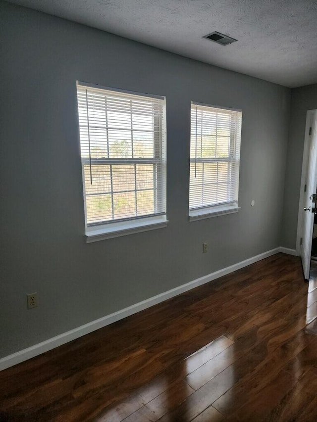 empty room featuring a healthy amount of sunlight, visible vents, dark wood finished floors, and baseboards