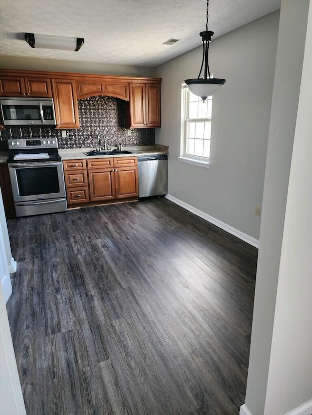 kitchen featuring brown cabinets, stainless steel appliances, backsplash, dark wood-type flooring, and a sink