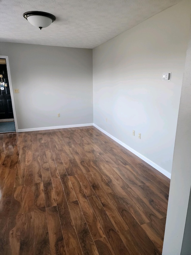 empty room with dark wood-style flooring, a textured ceiling, and baseboards