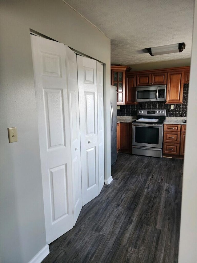 kitchen with decorative backsplash, dark wood finished floors, glass insert cabinets, stainless steel appliances, and a textured ceiling