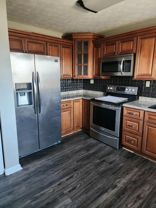 kitchen featuring stainless steel appliances, dark wood-style flooring, tasteful backsplash, brown cabinetry, and glass insert cabinets