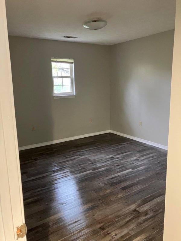 empty room with dark wood-style floors, visible vents, and baseboards